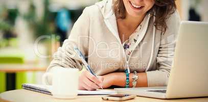 Cheerful student doing homework by laptop at cafeteria table