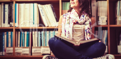 Thoughtful female student against bookshelf on library floor