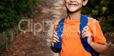 Smiling boy with backpack standing on the path in forest