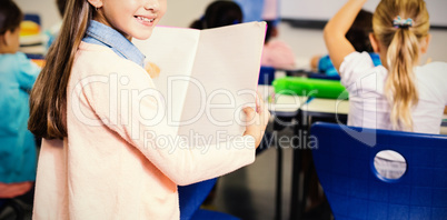 Portrait of schoolgirl standing with book in classroom