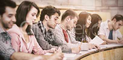 Students writing notes while sitting in row at lecture hall
