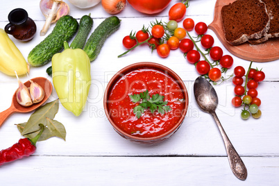 Soup gazpacho in a brown ceramic plate on a white wooden backgro