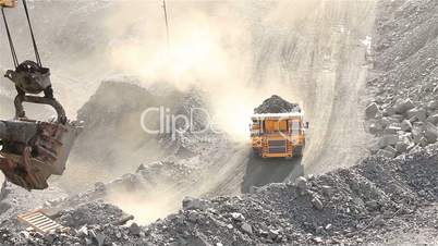 A truck with a full body of ore rides under the road in a large ore quarry