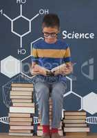 Student boy on a table reading against blue blackboard with science text and graphics