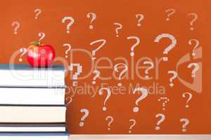 Books on the table against orange blackboard with question marks