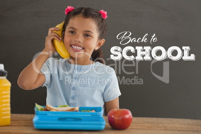 Happy student girl at table holding a phone against grey blackboard with back to school text