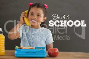 Happy student girl at table holding a phone against grey blackboard with back to school text