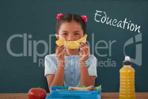 Composite image of girl holding banana at table