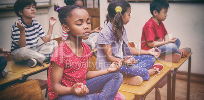 Pupils meditating in lotus position on desk in classroom