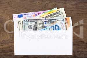 Dollars and euros in white envelop on wooden background.