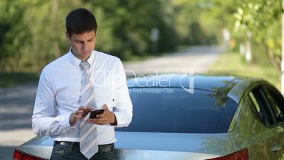 Young businessman browsing net with phone outdoors