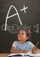 Happy student girl at table looking up against grey blackboard with A+ text