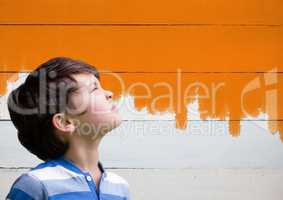 Boy looking upwards next to painted orange wall