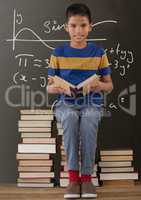 Happy student boy on a table reading against grey blackboard with education and school graphics