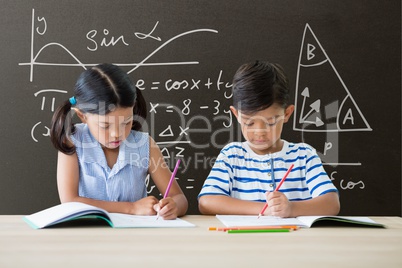 Students at table writing against grey blackboard with education and school graphics