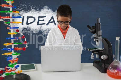 Student boy at table using a computer against blue blackboard with idea text