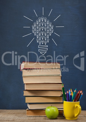 Books on the table against blue blackboard with bulb graphic