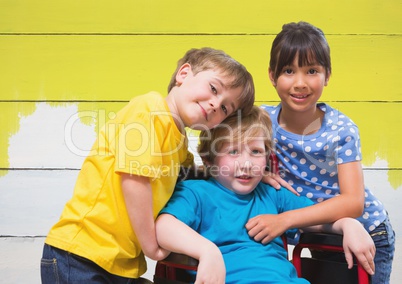 Disabled boy in wheelchair with friends with bright painted yellow wood background