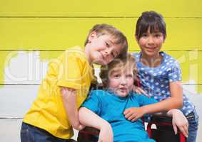 Disabled boy in wheelchair with friends with bright painted yellow wood background