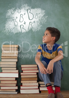 Student boy sitting on a table looking up against green blackboard with school and education graphic