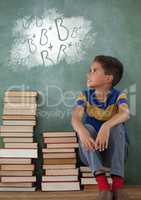 Student boy sitting on a table looking up against green blackboard with school and education graphic