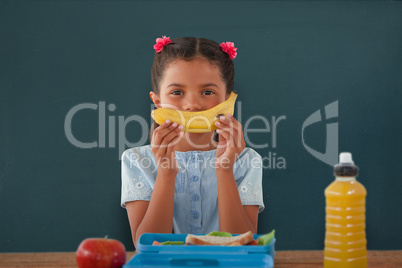 Composite image of girl holding banana at table