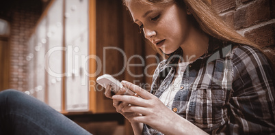 Student using smartphone sitting against wall