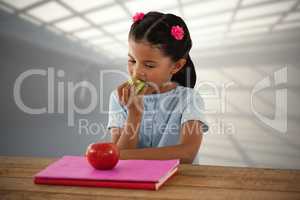 Composite image of girl eating granny smith apple at table