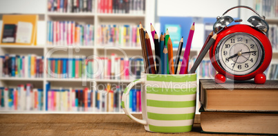 Composite image of books with alarm clock by colored pencils in mug on table