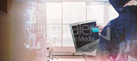 Composite image of rear view of hacker using laptop and credit card