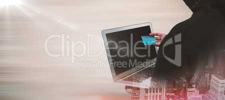 Composite image of rear view of hacker using laptop and credit card