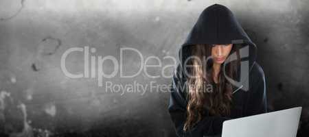 Composite image of female hacker in black hoodie using laptop