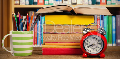 Composite image of stack of books by mug with colored pencils and alarm clock on table