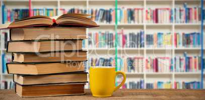 Composite image of stack of books by yellow mug on wooden table