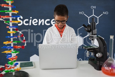 Student boy at table using a computer against blue blackboard with science text and graphics