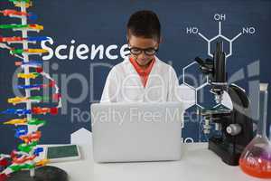 Student boy at table using a computer against blue blackboard with science text and graphics