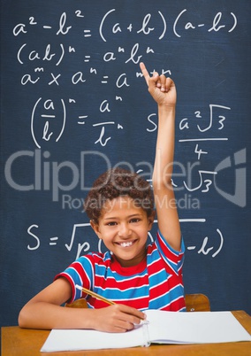 Happy student boy at table raising hand against blue blackboard with education and school graphics