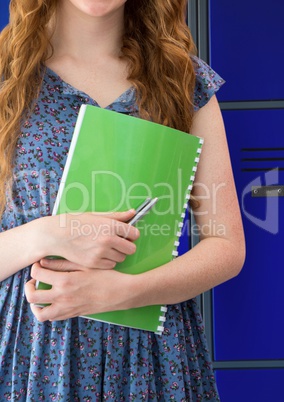 female student holding notepad in front of lockers