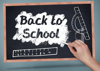 Hand writing back to school on blackboard with chalk and rulers