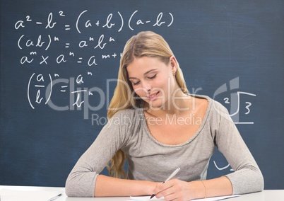 Student girl at table writing against blue blackboard with education and school graphics