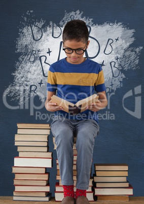 Student boy sitting on a table reading against blue blackboard with school and education graphic