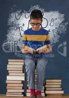 Student boy sitting on a table reading against blue blackboard with school and education graphic