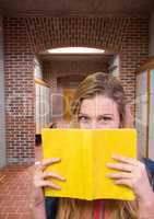 female student holding book in front of lockers corridor
