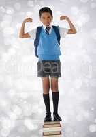 Schoolboy flexing strong arms while standing on books and bokeh bright background