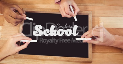 Hands writing back to school on blackboard