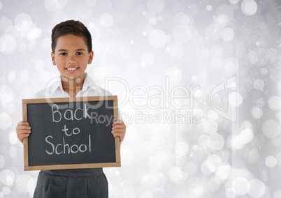 Schoolboy holding back to school blackboard in front of bright bokeh background