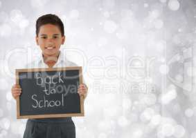 Schoolboy holding back to school blackboard in front of bright bokeh background
