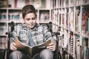 Disabled schoolboy reading book in library
