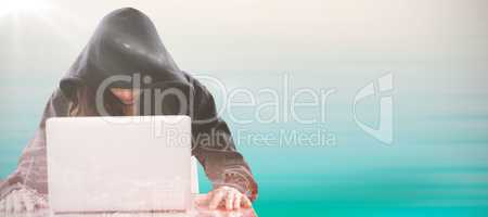 Composite image of female hacker sitting by laptop on table