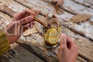 Cropped hand of woman adding cinnamon in lemon tea